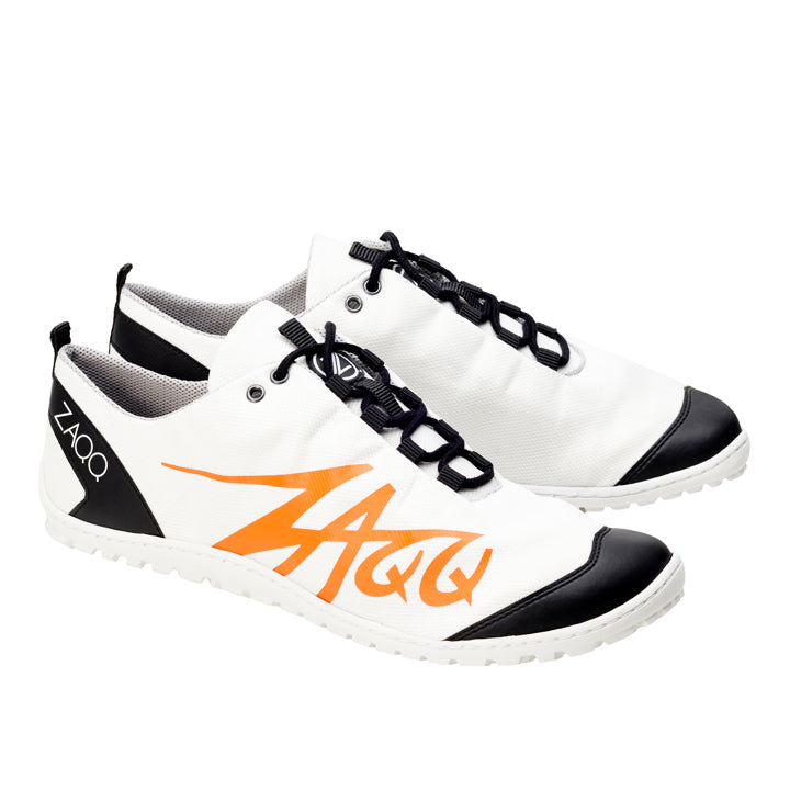 Die SQIM White Orange Sneaker von ZAQQ sind aus veganem Recycling-Gewebe gefertigt und verfügen über ein Barfußschuh-Design für natürlichen Komfort. Diese weißen Sportschuhe weisen schwarze Akzente auf, darunter schwarze schnürsenkelähnliche Verschlüsse und ein orangefarbenes ZAQQ-Logo an der Seite. Die Fersenlasche ist mit dem „ZAQQ“-Aufdruck verziert.