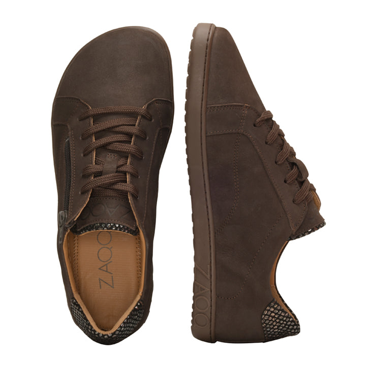 Entdecken Sie die QOMFY Wide Dark Brown Freizeitschuhe von ZAQQ aus hochwertigem Veloursleder. Diese minimalistischen Barfußschuhe zeigen ein strukturiertes Muster an Ferse und Sohle, wobei ein Schuh von der Seite und der andere von oben betrachtet wird. Das Design ist elegant mit einem sichtbaren Markenetikett auf der Innenseite versehen.