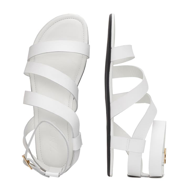 Wir präsentieren die MONIQ White Sandalen von ZAQQ: Diese atemberaubenden weißen Ledersandalen haben elegante überkreuzte Riemen und eine goldene Schnalle. Eine Sandale ist von oben und die andere von der Seite zu sehen, wodurch die flache Sohle und die schicken Knöchelriemen hervorgehoben werden. Damit sind sie perfekt für alle, die minimalistischen Stil schätzen.