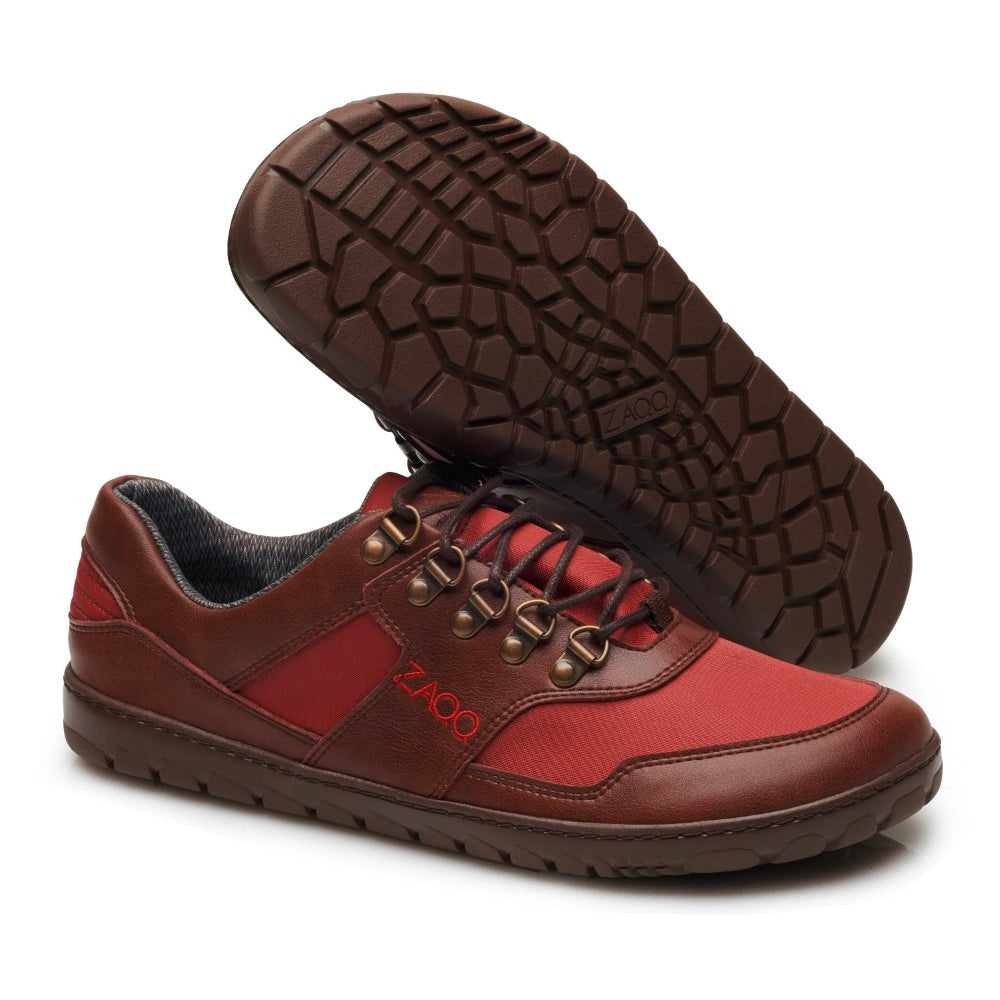 Die wasserdichten Wanderschuhe HIQE Low Vegan Camel Red von ZAQQ haben ein rot-braunes Design mit schwarzen Schnürsenkeln und strukturierten braunen Sohlen. Auf der Seite ist der Markenname „ZAQQ“ deutlich zu sehen. Ein Schuh steht aufrecht, während der andere geneigt ist, wodurch das komplizierte Profilmuster hervorgehoben wird. Ideal für alle, die ein lässiges und dennoch langlebiges Outdoor-Erlebnis suchen.