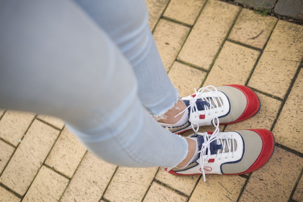 Eine Person in hellblauer Jeans und den leuchtenden weißen QOLETTE-Sneakern von ZAQQ steht selbstbewusst auf einem gelben Backsteinweg.