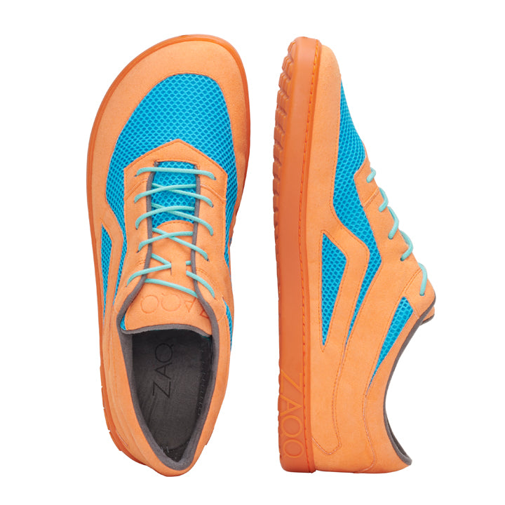 Der QLAYTON Orange Barfuß-Sneaker von ZAQQ besticht durch eine lebendige Kombination aus Orange und Blau. Der linke Schuh aus Veloursleder zeigt eine Draufsicht mit Schnürdesign und Mesh-Textur. Der rechte Schuh wird von der Seite gezeigt und hebt seine Profilsohle und das stylische Muster hervor.