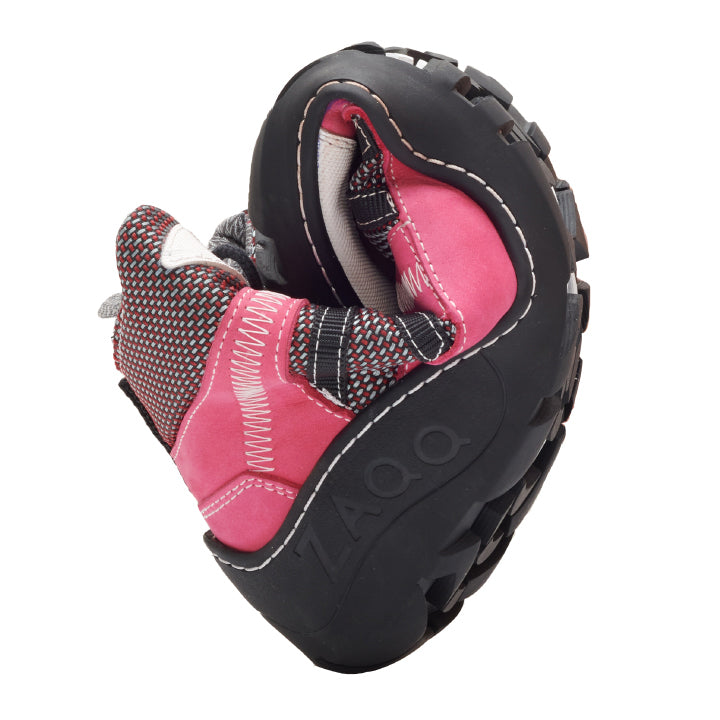 Der RUQQ Rosa Waterproof von ZAQQ ist ein flexibler pink-schwarzer Outdoor-Barfußschuh, der sich leicht drehen lässt, um seine Biegsamkeit zu demonstrieren. Er verfügt über eine robuste, rutschfeste Sohle mit sichtbaren Nähten und dem ZAQQ-Logo, während der obere Teil verschiedene Texturen und Muster wunderschön kombiniert.