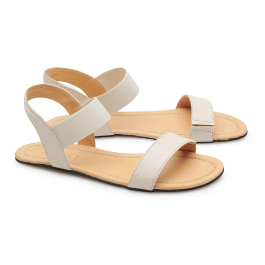 Die SLIQ Beige Sandalen von ZAQQ bestechen durch ihr minimalistisches Design mit zwei breiten Riemen über dem Fuß und einem Knöchelriemen für mehr Komfort. Diese Barfußsandalen haben eine flache Sohle und sind auf einem strahlend weißen Hintergrund für einen sauberen Look abgesetzt.