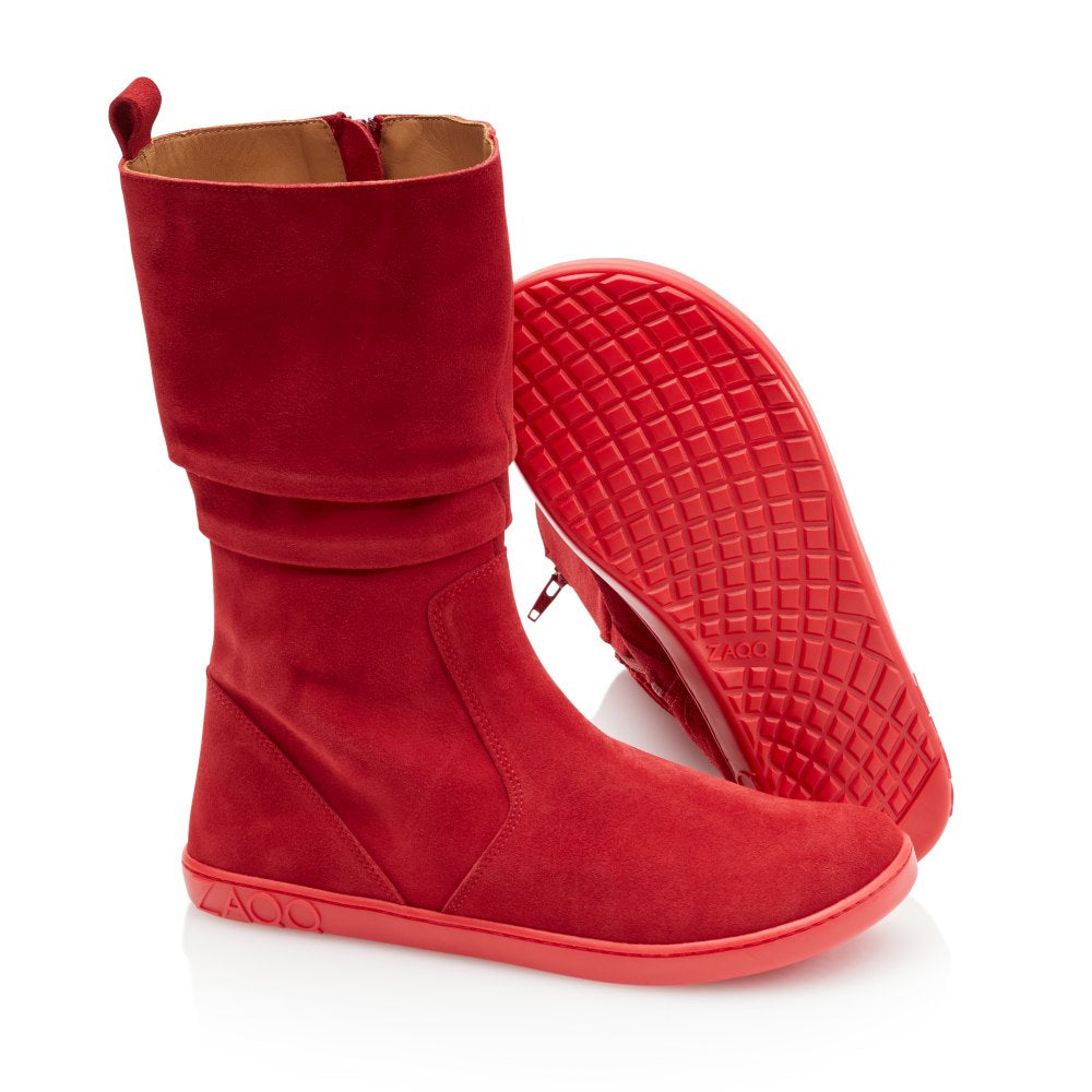 Wir präsentieren den ZAQQ QOM Red: Ein Paar rote Stiefel aus Ziegenveloursleder mit flachen Sohlen. Ein Stiefel steht aufrecht, während der andere sich neigt, um das Profilmuster zu zeigen. Diese Stiefel haben ein leicht lässiges Obermaterial und einen seitlichen Reißverschluss und bieten eine atmungsaktive Passform, die perfekt für diejenigen ist, die den Komfort eines Barfußschuhs schätzen.