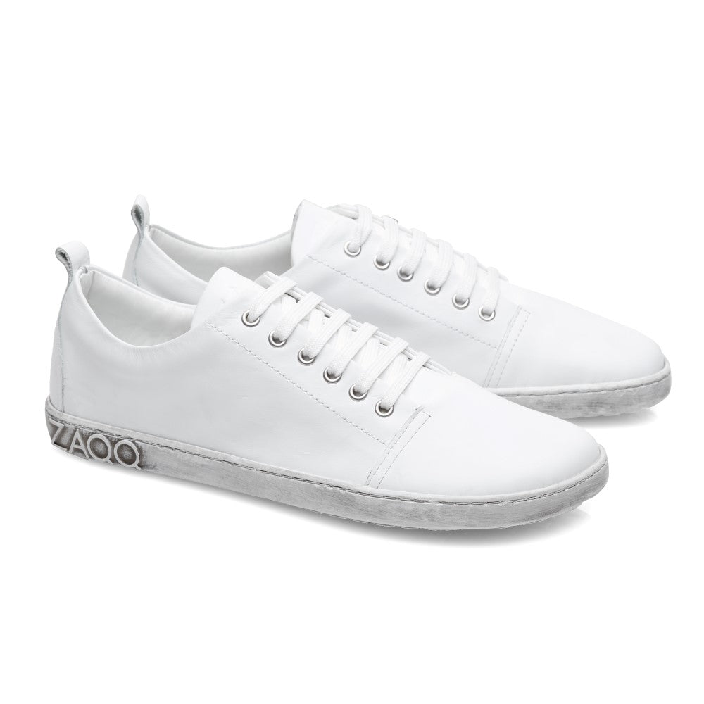 Die TAQQ Nappa White Low-Top Sneaker von ZAQQ bestechen durch cleanes, weißes Nappaleder mit weißen Schnürsenkeln und einer Kautschuksohle. Ihre Sohlen sind mit einem stilisierten Textdesign verziert, das sowohl in der Seiten- als auch in der Schrägansicht präsentiert wird.